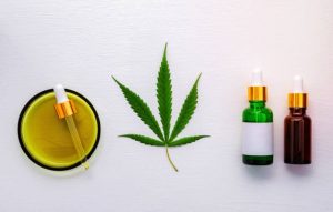 Glass bottle of cannabis oil and hemp leaves set up on white background.