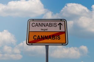 A sign with the text legal cannabis and an arrow pointing up over the crossed-out word cannabis against a cloudy sky