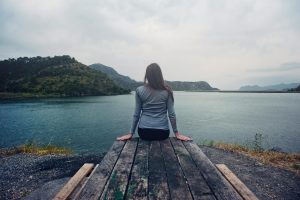 A lady sitting by the edge of a shoreline. blue body of water