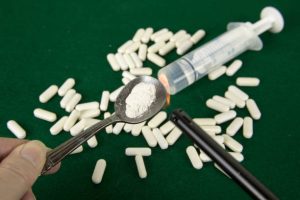 Crushed powdered opioids in spoon with lighter, pills and syringe.