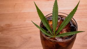 glass of cola with cannabis leaf and ice cubes