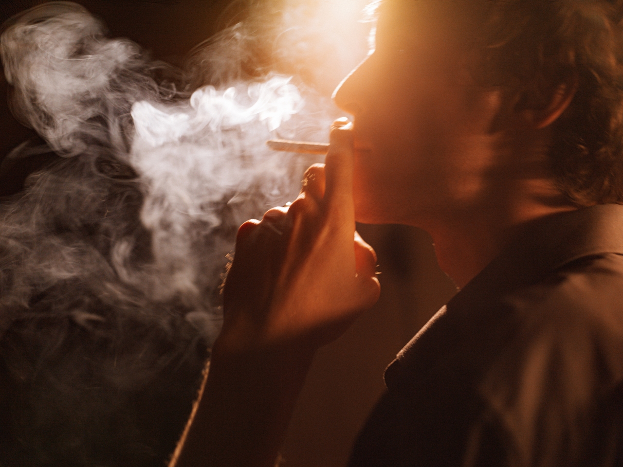 man smoking a joint with smoke covering his face