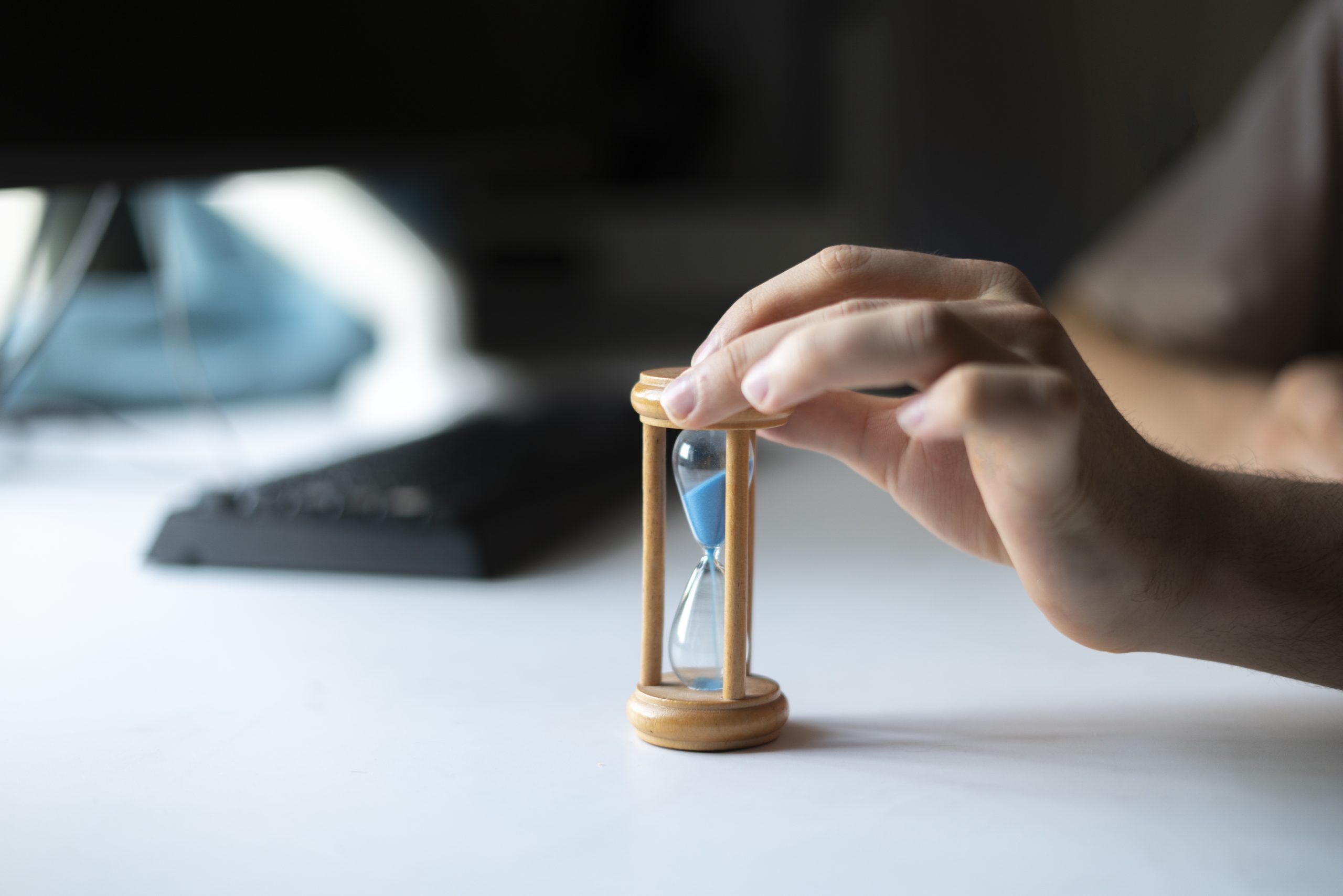 businessman sitting on the workplace, hand holding hourglass as the time is money concept