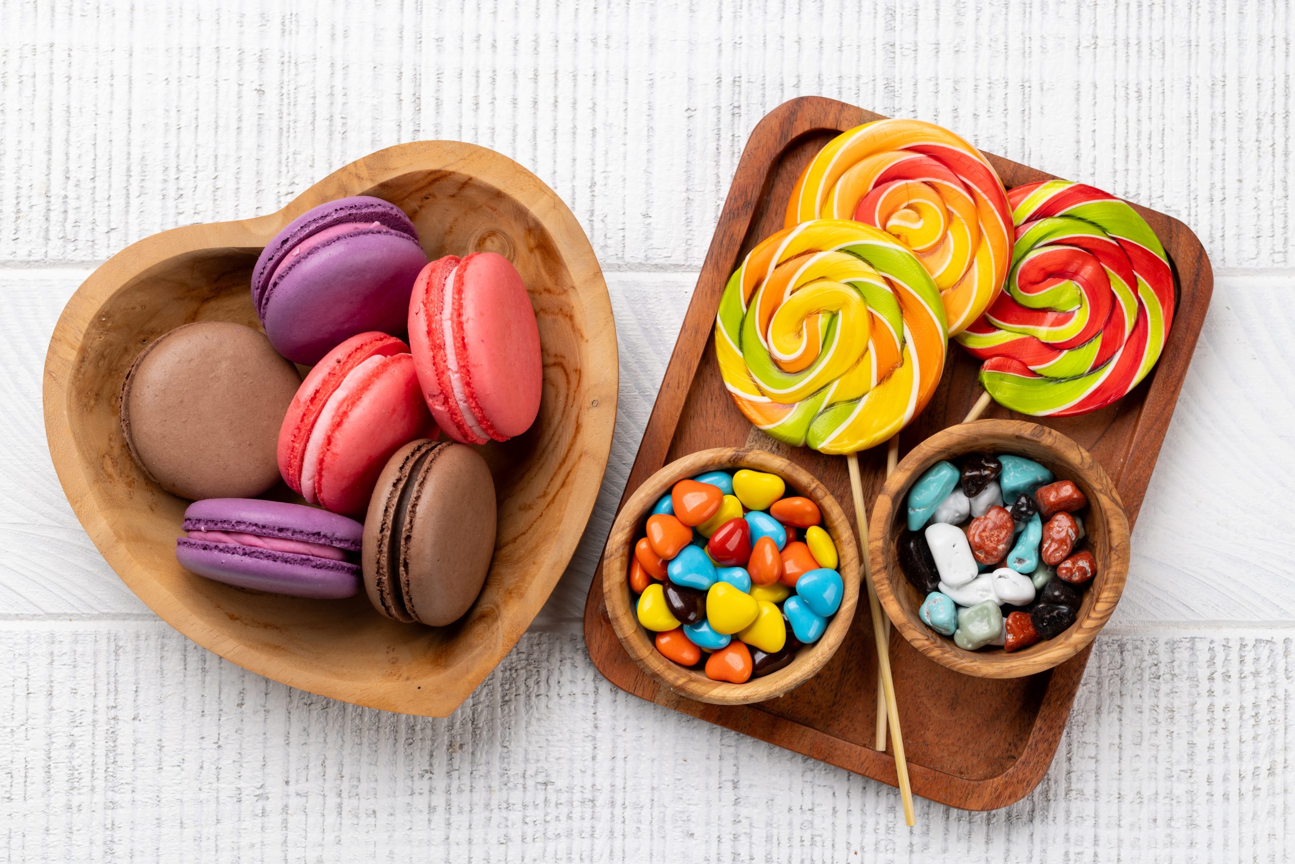 Various colorful candies, lollipops, and macaroons. Flat lay over wooden background